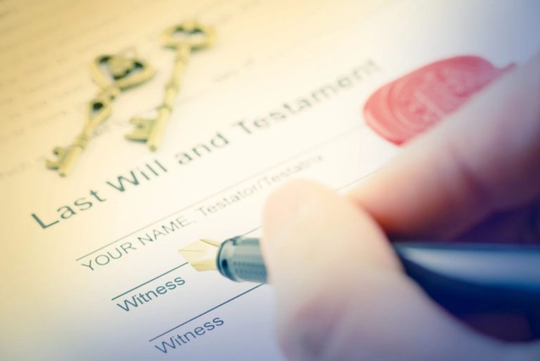 Close-up of a person signing a Last Will and Testament document with antique keys placed on the paper, symbolizing estate planning and inheritance.