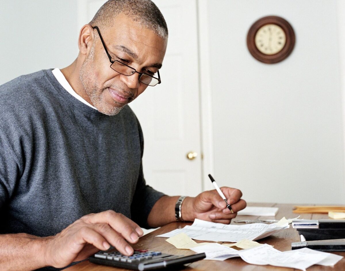 Focused man using a calculator and reviewing paperwork at a table, representing the importance of tax planning and estate planning during uncertain financial times.