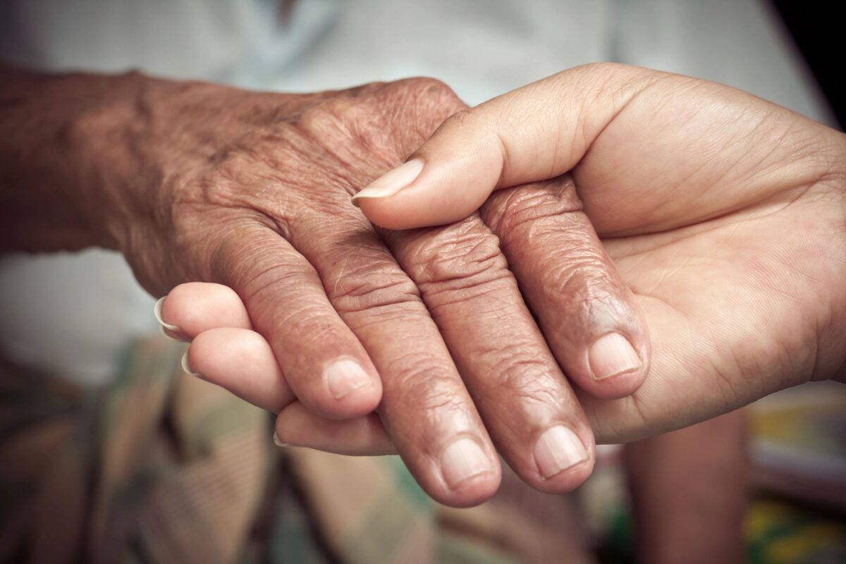 Close-up of caregiver gently holding an elderly person’s hand, symbolizing dementia care and support