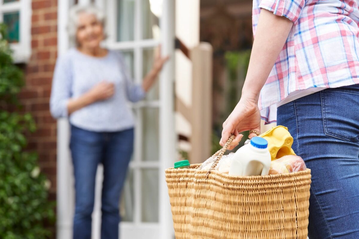 A person carrying groceries to an older adult’s door, symbolizing safe and supportive shopping for seniors.